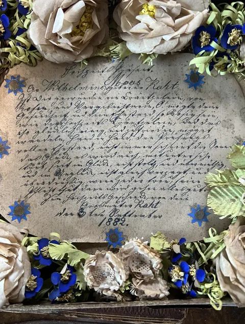A handwritten German wedding greeting dated 1882, surrounded by a handmade wreath of paper roses and blue forget-me-nots