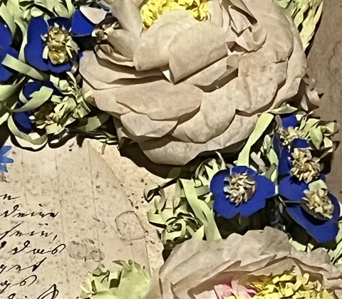 Close detail of handmade paper roses and blue paper forget-me-nots, each blue flower centred with a dried natural flower head