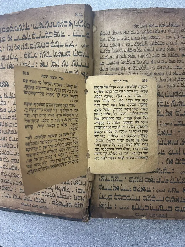 Loose printed leaves in square Hebrew type with vowel points, lying on top of the hand-written pages of a different book