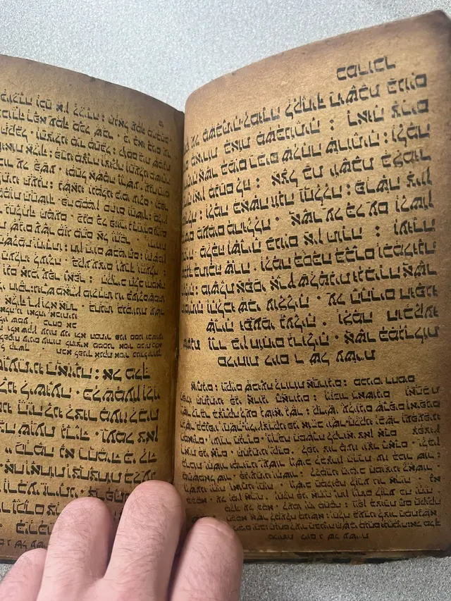 An open hand-written book showing dense right-to-left script in rounded connected letterforms on heavily browned paper